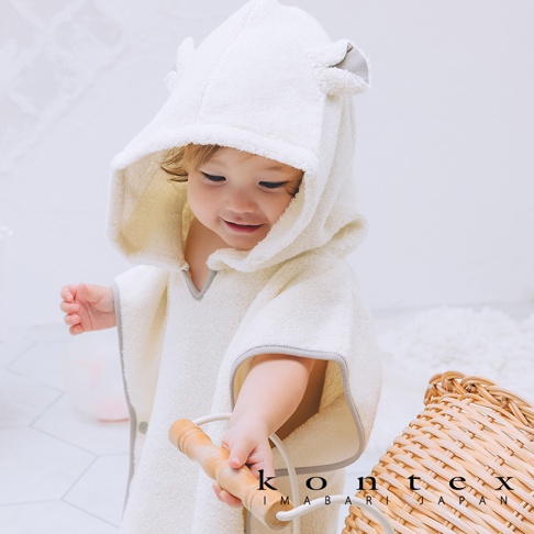 嬰兒穿著奶油白色、帶有熊耳造型連帽的浴巾斗篷，材質為柔軟的毛巾布，連帽和斗篷邊緣飾有灰色滾邊。