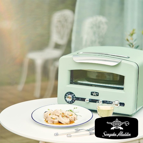 日本千石阿拉丁 320 度極炙烤箱三代旗艦款，搭配一盤精緻的烤肉捲和一杯飲品，擺放在戶外餐桌上。