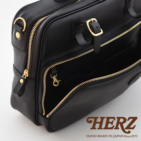 黑色皮革兩用商務公事包，附有金色拉鍊和扣環，包身結構挺立，展現精緻工藝。