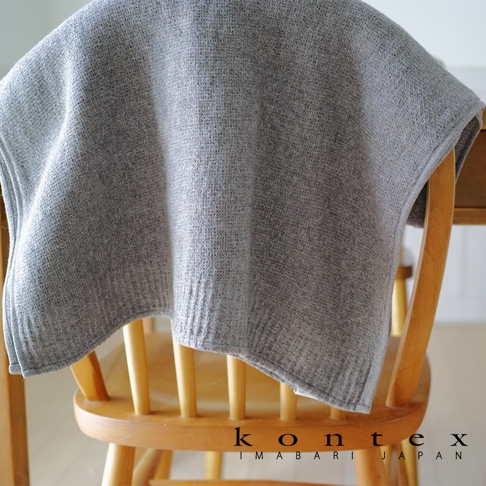 一塊淺灰色針織紋理的純棉毛巾，懸掛在木質椅背上，毛巾邊緣帶有羅紋織法。