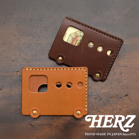 HERZ 品牌皮革製作的巴士造型零錢包，一個為深棕色，內有彩色印刷圖案；另一個為淺棕色，細緻縫線與金屬鉚釘點綴，展現職人手作質感。