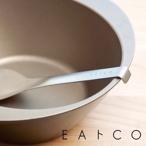 日製服務餐匙，金屬材質，呈現銀色光澤，匙柄上印有「EATCO」字樣，置於一個淺棕色、帶有光滑內壁的碗中。