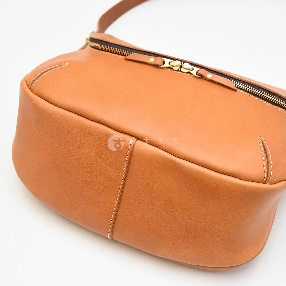 一個棕色皮革包的局部特寫，上面有金色的拉鍊和白色縫線。