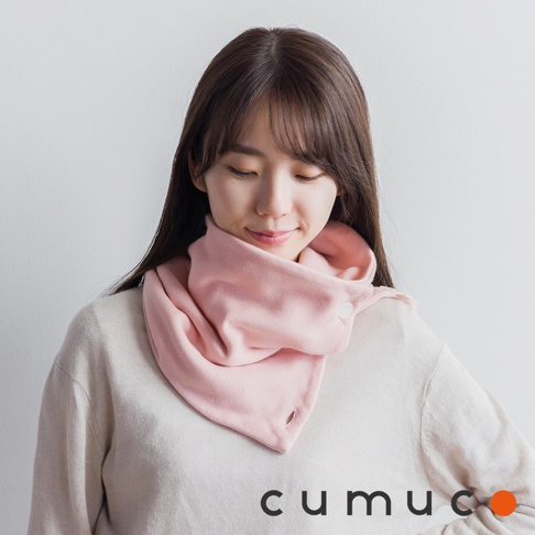 一個穿著米色毛衣的年輕女子，戴著粉紅色的圍巾，圍巾上有兩個白色鈕扣，圍巾上印有 CUMUCO 的品牌名稱。