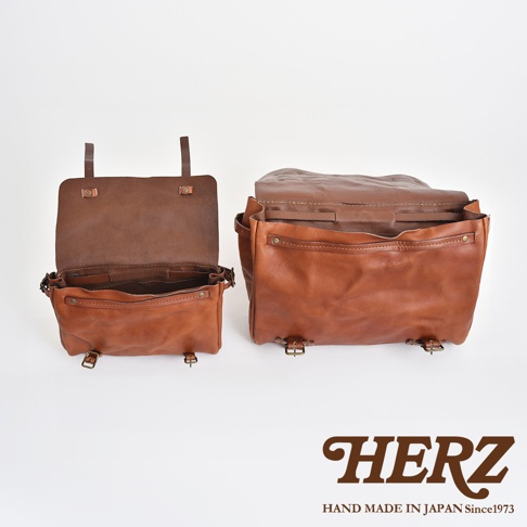 兩款棕色皮革復古郵差包，其中一款敞開展示內部，兩款皆有金屬扣環與皮帶裝飾。