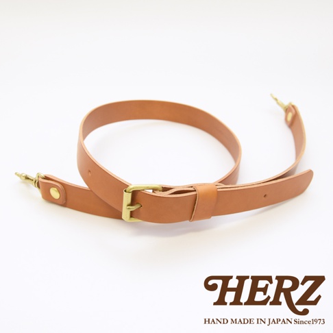 咖啡色皮革製成的可調式肩背帶，附有金色金屬扣環和鉤子，底部印有 HERZ 字樣和 HAND MADE IN JAPAN Since1973 字樣