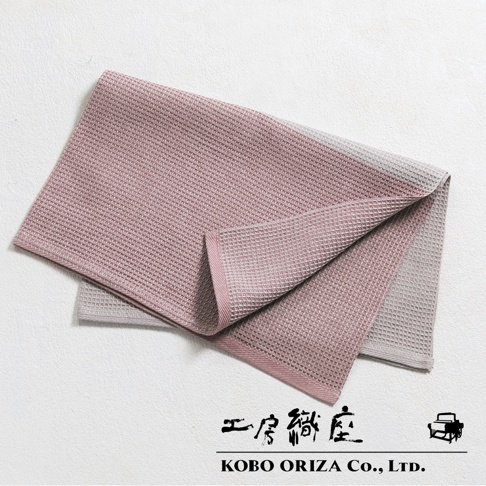 粉色與灰色雙色棉麻混紡拭巾，表面有鬆餅紋理，邊緣有粉色滾邊。