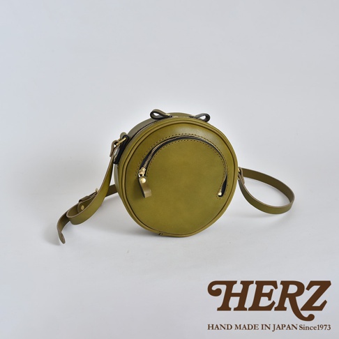 橄欖綠皮革小圓包，圓形設計，正面有拉鍊隔層，附可調節肩帶和提把，材質為皮革，風格簡約。