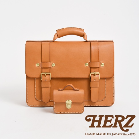 兩個棕褐色皮革包，一個較大，一個為迷你尺寸，皆有翻蓋、皮帶扣和提把設計。