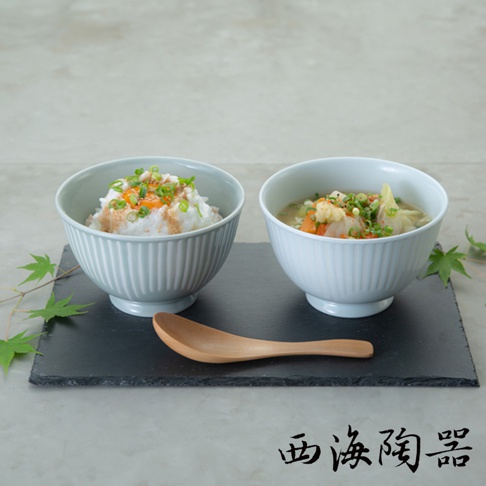 兩只波佐見燒飯碗，一個盛有飯和配料，另一個裝有湯品，碗身有細緻的豎條紋，呈淺藍色和白色，搭配木質湯匙，置於黑色石板上。