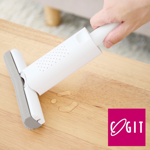 白色推拉海綿刷，帶有灰色海綿頭，置於木質檯面上，旁邊有幾滴水珠。