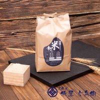 一個棕色紙袋裝著北海道七星米2公斤，袋頂繫著麻繩。袋上有深藍色標籤，標示著「現職米」和「幸」字樣，以及其他產品資訊。一旁有一個木盒裝著白米，背景是木紋和麥穗。