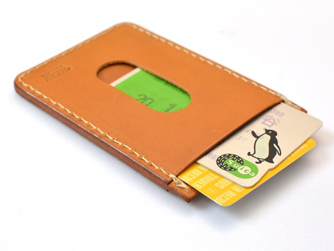 職人手作皮革直式票券收納夾，淺棕色皮革，側邊縫線。夾內可見一張綠色票券、一張印有企鵝圖案的卡片及一張黃色卡片。