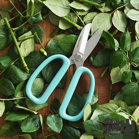 日本霜山加寬舒適握柄園藝剪刀，置於滿是綠葉和樹枝的木質背景上。