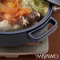 海軍藍陶土湯鍋內燉煮著香菇、貢丸、紅蘿蔔片與白菜，鍋身呈現光滑質地，配有兩側深藍色把手，置於電磁爐上，爐面顯示加熱指示燈。