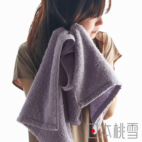 一位女子用淡紫色毛巾擦拭臉部，毛巾材質蓬鬆柔軟，可見一旁有「日本桃雪」的品牌標誌。