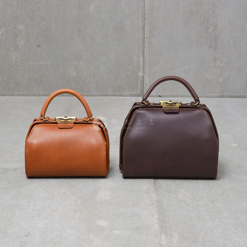 兩款職人手作皮革Organ兩用口金手提包，左為焦糖色，右為深棕色，皆為方形造型，配有提把及金色金屬口金。