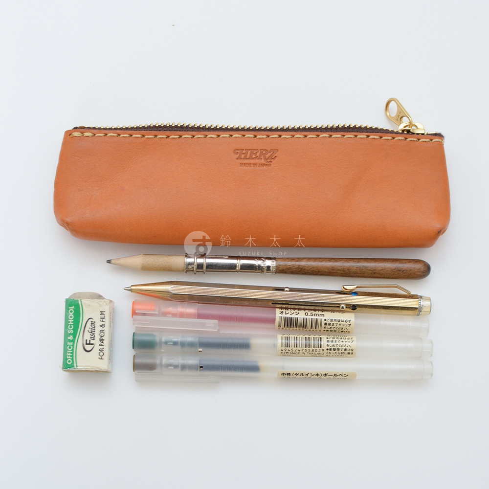 職人手作皮革經典收納筆袋，淺棕色皮革材質，配有金色拉鍊。筆袋旁擺放一支木質鉛筆、一支金色金屬筆、橡皮擦以及數支不同顏色的透明筆身簽字筆。