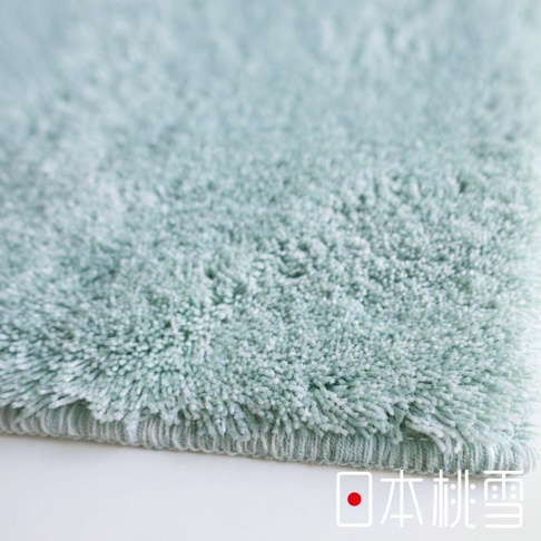 淺綠色絨毛地毯的細節特寫，底部有日本桃雪的品牌標誌。