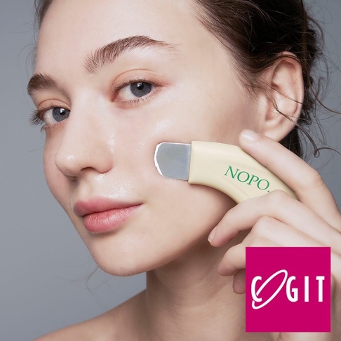 淡黃色 NOPO. 毛孔清潔柔滑角質淨膚棒，銀色金屬刮片，正被女性手指握住，輕貼臉頰。