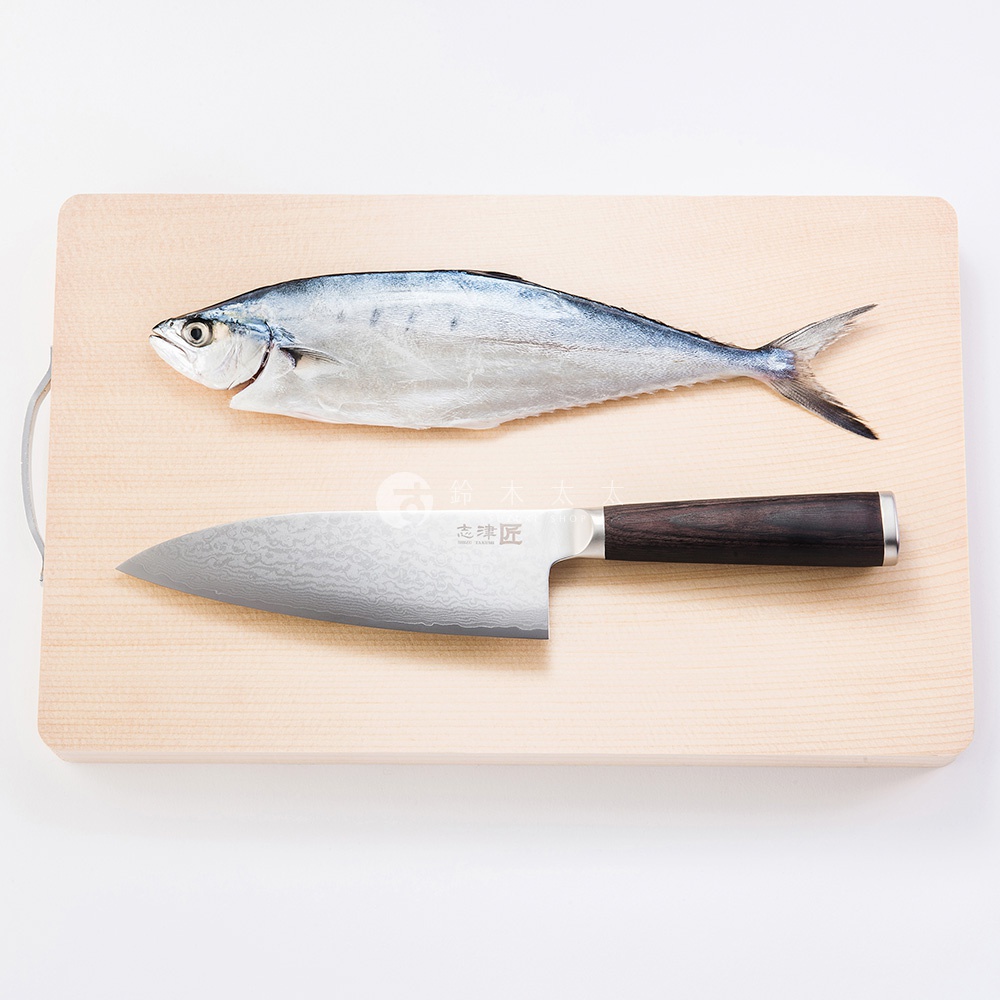 木質砧板上，一條銀色魚身，搭配一把不鏽鋼主廚刀，刀刃呈現大馬士革紋路，刀柄為深棕色木質。