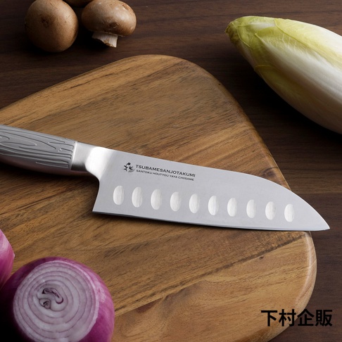 鉬釩不鏽鋼三德刀，刀柄為銀灰色，帶有木紋飾，刀身為銀色，飾有圓形凹槽和品牌標誌，放置於木質砧板上，周圍有洋蔥和蘑菇。