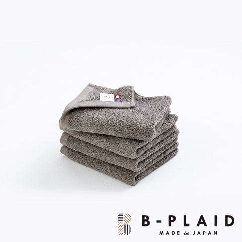 一疊深灰色毛巾，帶有細緻的鱗紋織紋，材質為棉，頂部毛巾左上角有一個帶有品牌標誌的織標。