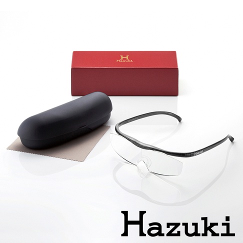 Hazuki 品牌的紅色眼鏡盒、黑色眼鏡盒、灰色拭鏡布和黑框放大鏡，上面印有 Hazuki 字樣。