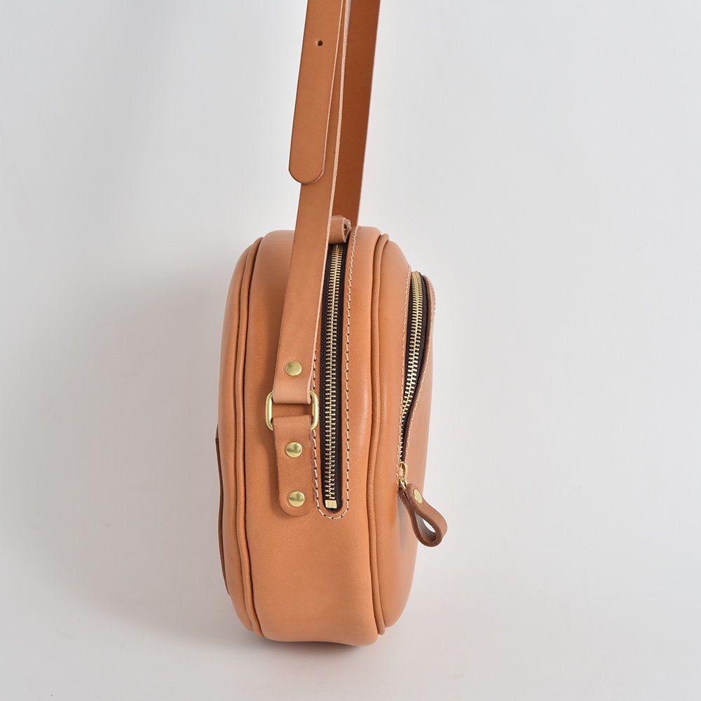 職人手作皮革小圓包 CK-19 M，淺棕色，採用天然皮革製成，配有兩個拉鍊開口和可調節的肩帶，整體呈現圓潤飽滿的造型。