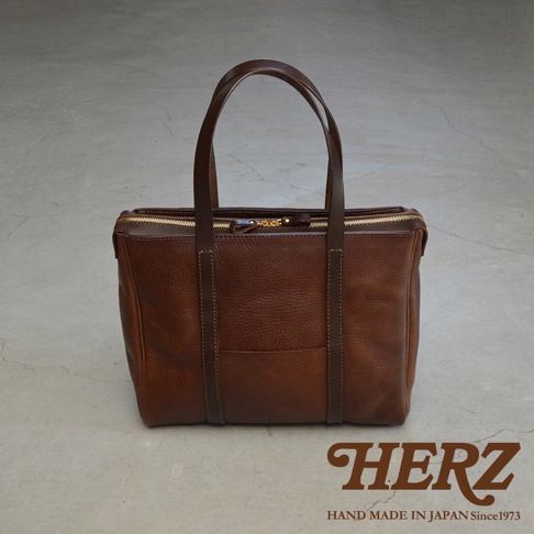 棕色皮革製成的職人手作Organ肩背拉鍊托特包，帶有雙提把和金色拉鍊，包身中央有縫線裝飾，質感樸實。