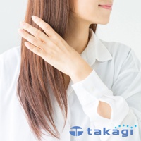 一名女子穿著白色襯衫，用手整理一頭褐色長髮。襯衫袖口鈕扣和品牌 Logo「takagi」標示於畫面右下方。