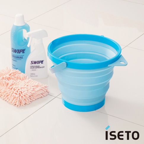 淺藍色可伸縮旅行水桶，帶有藍色提把和邊緣，由矽膠材質製成。旁邊有兩瓶清潔劑和粉紅色絨毛布。