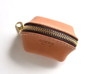 一個棕色皮革製貝殼造型零錢包，配有金色拉鍊和皮革拉環，表面有「HERZ」壓印。