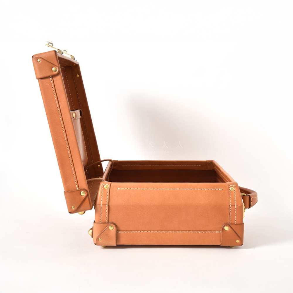 一個開啟的淺棕色皮革手提箱，帶有金色金屬細節和白色縫線。