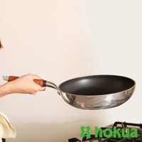 一只手握著一個不鏽鋼材質、帶有天然木柄的輕量炒鍋，鍋內為黑色。