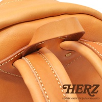 職人手作皮革後背包，皮革呈現溫潤的淺棕色，帶有細緻的縫線與金屬扣件，展現皮革的紋理與質感。