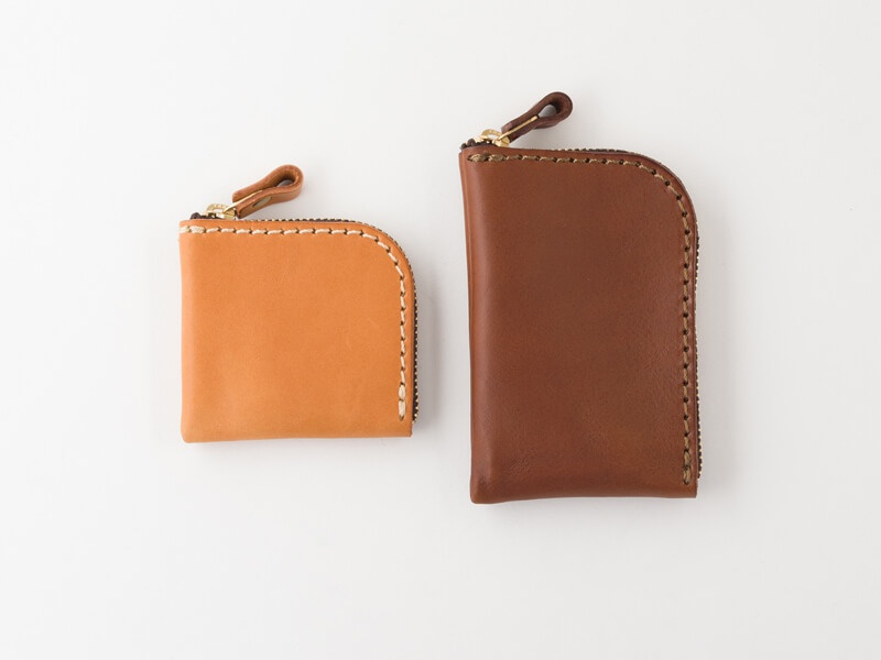 職人手作皮革分隔收納零錢包，一個為淺棕色，另一為深棕色。兩款零錢包均為 L 型拉鍊開口，使用植鞣皮革製作，縫線精緻，附有皮革拉頭。