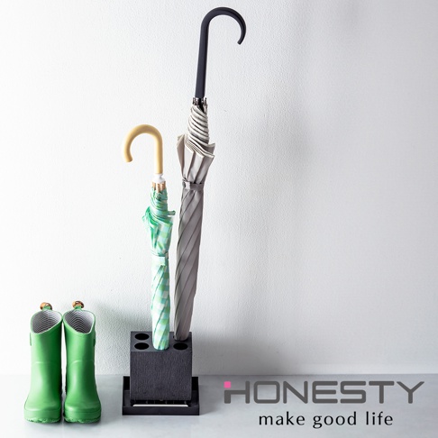 深色珪藻土傘架，可拆卸設計，擺放兩把雨傘，一把為綠色格紋，另一把為灰色，傘架旁有兩雙綠色雨靴。