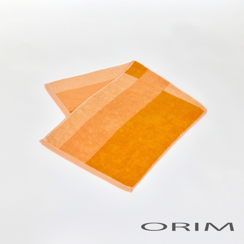 一條橘色漸層的毛巾，由深橘色、淺橘色與亮橘色組成，材質為柔軟的棉，呈現簡約的色塊拼接設計。