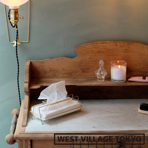 黃銅色金屬線條構成的收納面紙盒，內有白色面紙，上方有部分面紙抽出，置於大理石檯面上。