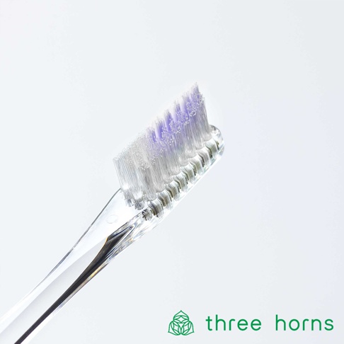 透明塑膠手柄，尖頭設計，帶有白色和紫色柔毛的牙刷特寫。