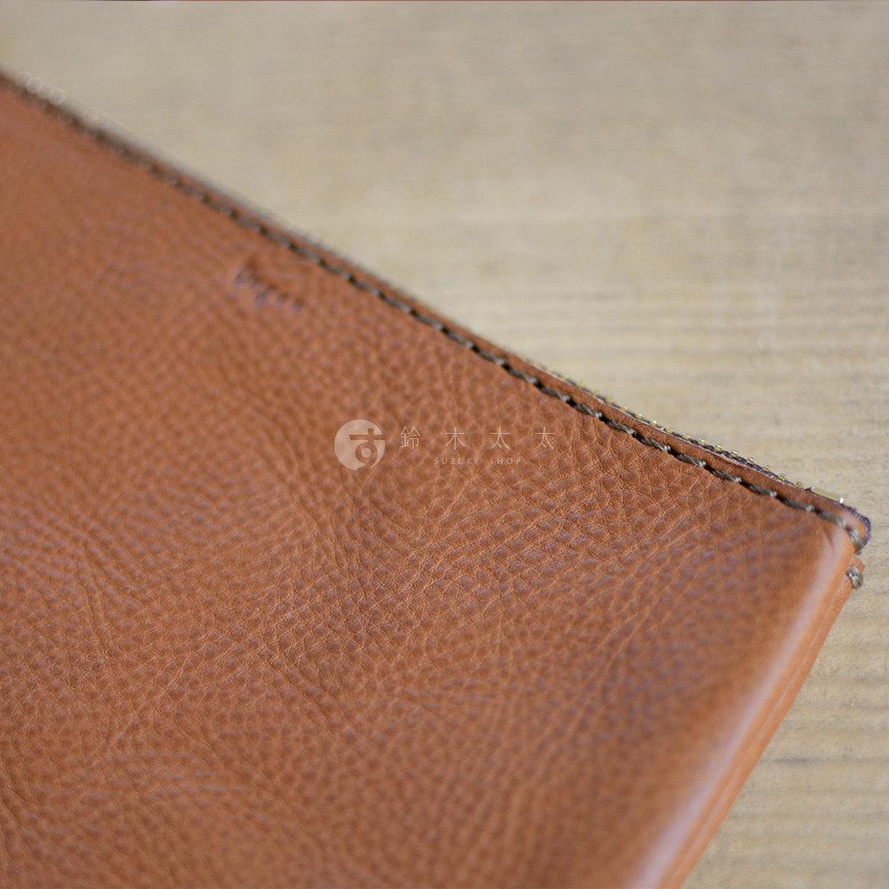 職人手作皮革Organ拉鍊式小物收納袋，特寫展示棕色皮革的紋理與縫線細節，袋身一角有品牌Logo。