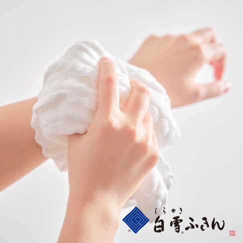 雙手正拿著一條白色、質地柔軟的沐浴巾，沐浴巾呈現輕柔蓬鬆的觸感，邊緣有明顯的縫線。