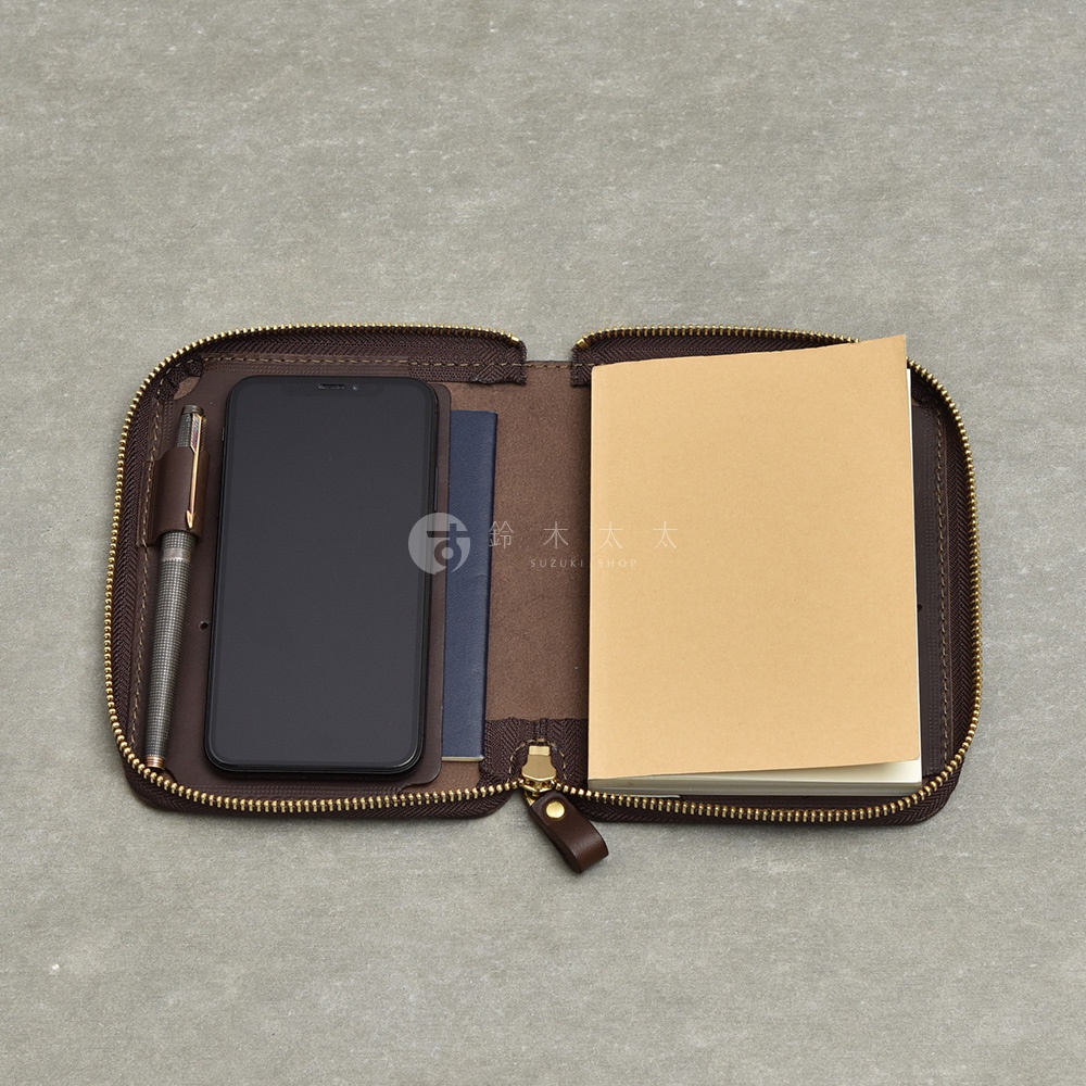 職人手作皮革Organ記事本收納包，內部包含手機、護照夾層，以及一本筆記本，整體為深棕色皮革材質，搭配金色拉鍊。