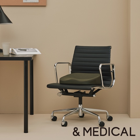 黑色辦公椅上放置著一個綠色低反發美姿支撐坐墊，坐墊呈現人體工學的弧形設計。