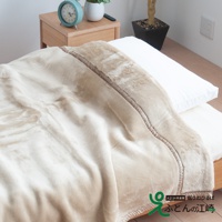 米白色加厚柔暖毯，絨毛材質，邊緣有深棕色滾邊與縫線裝飾，鋪在床上，搭配白色枕頭，營造溫馨氛圍。