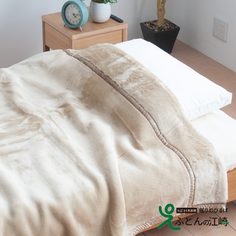 米白色加厚柔暖毯，絨毛材質，邊緣有深棕色滾邊與縫線裝飾，鋪在床上，搭配白色枕頭，營造溫馨氛圍。