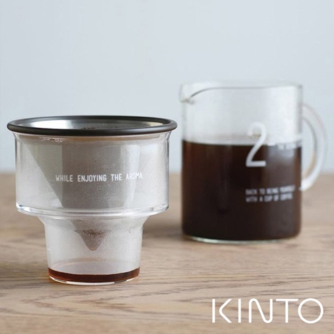 透明玻璃濾杯組，內含金屬濾網，印有英文文字；搭配裝有深色咖啡的透明玻璃分享壺，壺身印有白色數字「2」，整體置於木質桌面。