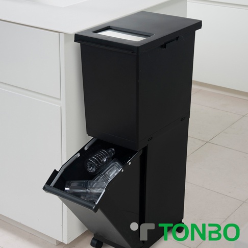 黑色雙層塑膠分類垃圾桶，上方有方形投放口，下方抽屜式收納設計，內有透明塑膠瓶，垃圾桶底部有輪子方便移動。