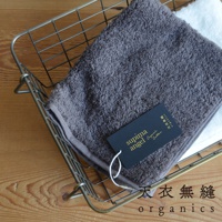 金屬籃子內放著一條深灰色、蓬鬆柔軟的匹馬棉毛巾，旁邊疊著一條白色毛巾。毛巾上有一個黑色吊牌，印有金色「supima angel Organic Cotton」字樣。